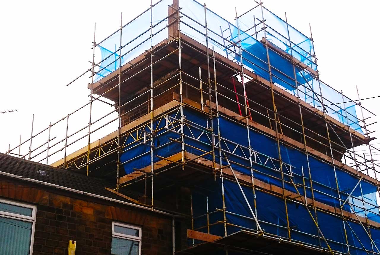 distance view of a sheffield domestic brick built home part way through a lost conversion wrapped in scaffold allowing tradesmen to work