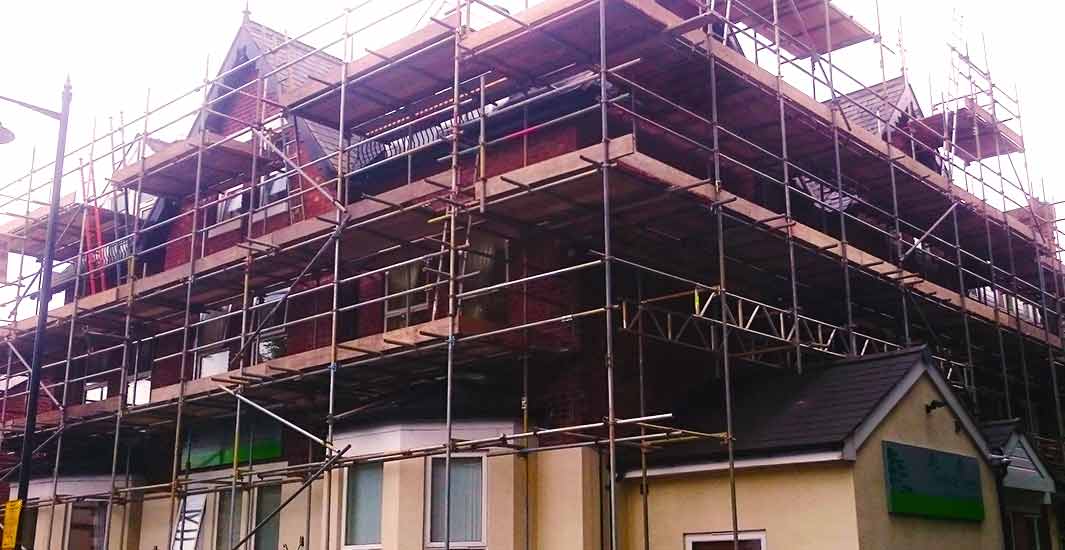 distance photo of a scaffold expert inspecting a building with scaffold erected all the way around a large new build sheffield property